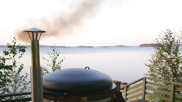 A wood-burning stove on a deck overlooking a calm lake. - SResort Sauna Villas (Lappeenranta)