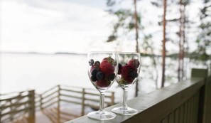 Two glasses of fruit on a wooden railing with a view of the water and trees in the background.