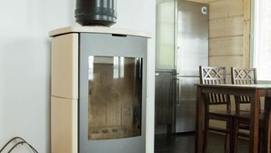 A modern kitchen with a wood-burning stove, a refrigerator, and a dining area with chairs. - SResort Sauna Villas (Lappeenranta)