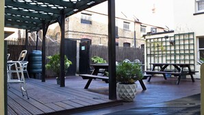 An outdoor patio area with picnic tables and chairs, a wooden deck, and a water tank. - The Hope Hotel (Southend-on-Sea)