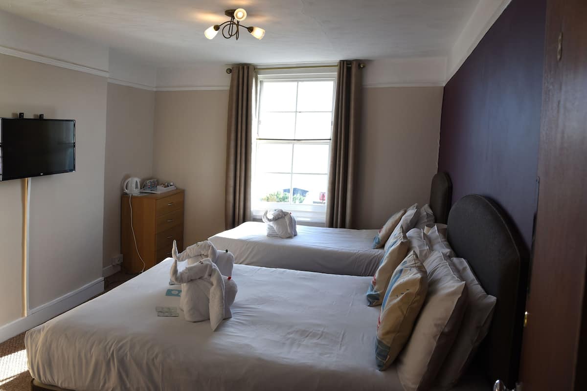 A hotel room with two beds, a television, a minibar, and a window with curtains.
