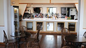 A bar area with multiple tables and chairs, a refrigerator, and various bottles and glasses on the counter. - The Hope Hotel (Southend-on-Sea)