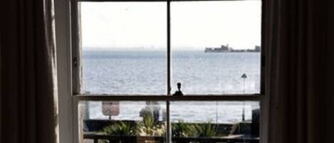 A window with a view of the sea and a distant ship.