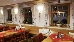 Un restaurant avec des tables et des bancs en bois, décoré de nappes rouges et de coussins blancs.