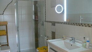 Une salle de bain avec une douche à parois de verre, des toilettes avec un abattant jaune, un lavabo avec un miroir et un porte-serviettes.