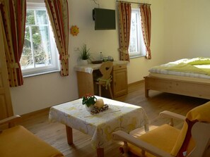 A cozy room with a bed, a desk with a chair, a small table with a plant, and a window with curtains. - Gasthof Engel (Bad Wurzach)