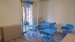 Ein Zimmer mit einem Holzkasten, einem blauen Tisch mit Stühlen und einer Glasschiebetür, die auf einen Balkon führt.