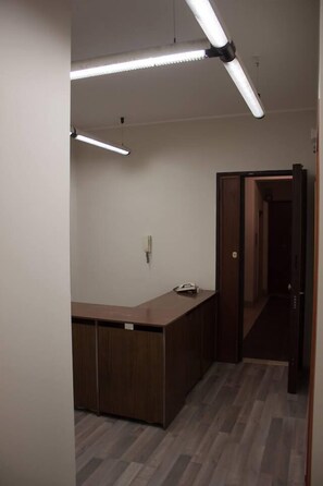 A hallway with a wooden desk, fluorescent lighting, and a door leading to another room. - Seaside & City (Catania)