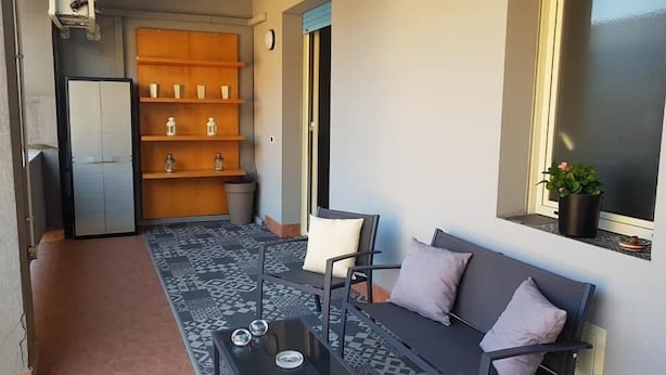 Ein Balkon mit einer Couch, einem kleinen Tisch und einem Regal mit Dekorationen.