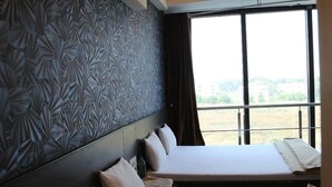 Habitación de hotel con dos camas, un papel tapiz estampado, un equipo de aire acondicionado y un ventanal con vistas.