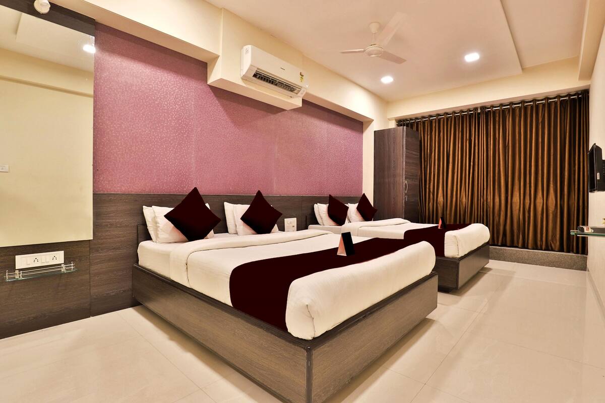 A modern hotel room with a large bed, a ceiling fan, an air conditioning unit, and a view of the city through curtains.