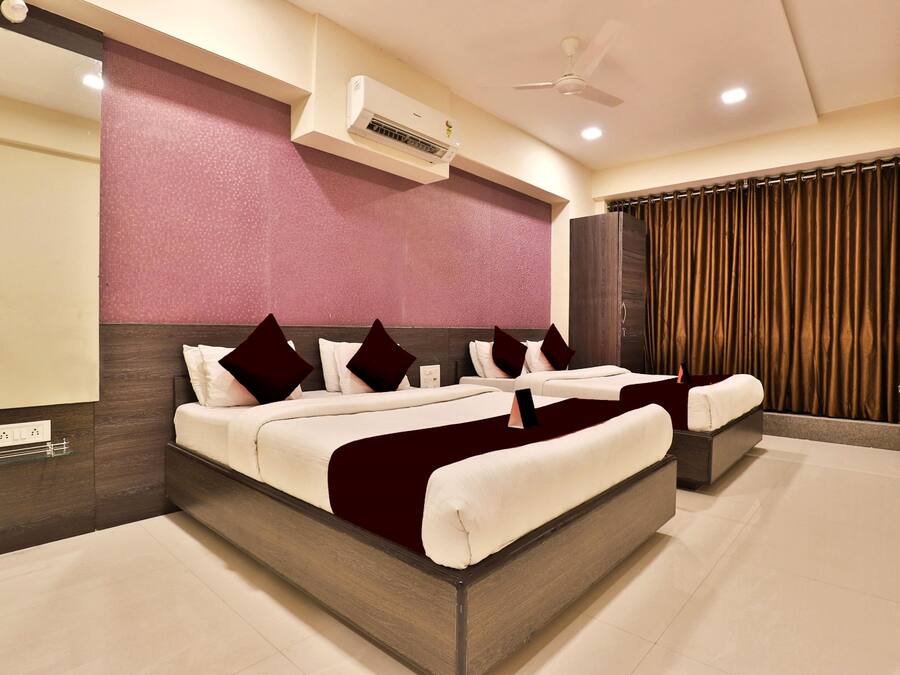A modern hotel room with a large bed, a ceiling fan, an air conditioning unit, and a view of the city through curtains.