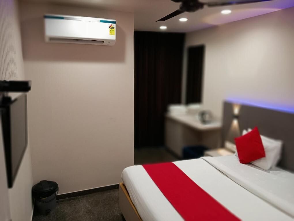 A hotel room with a bed, a ceiling fan, an air conditioning unit, and a small desk with a chair.
