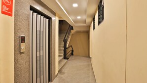 Un pasillo con una cámara de seguridad, un panel de control digital para el ascensor y una escalera.