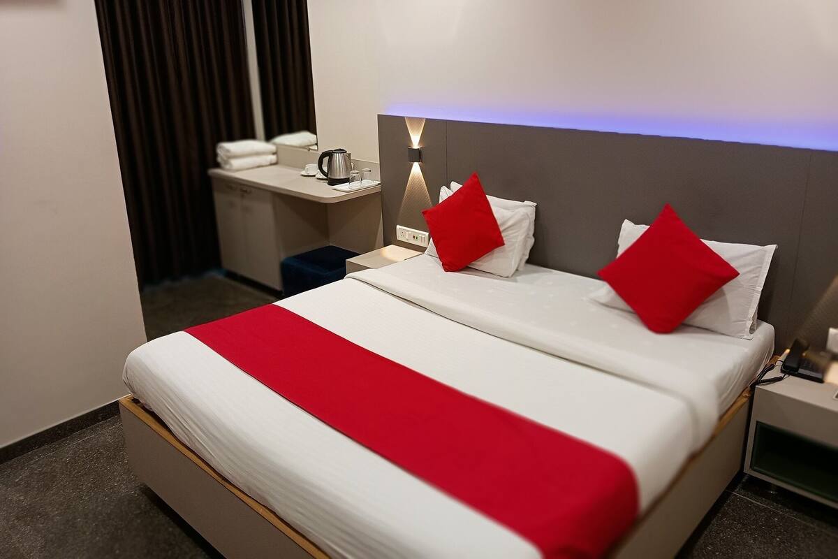 A hotel room with a bed, bedside table, and a small desk with a kettle.