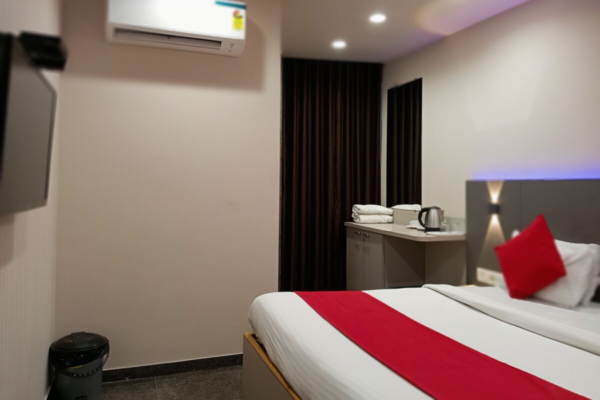 A hotel room with a bed, a desk, an air conditioning unit, a trash bin, and a mirror.