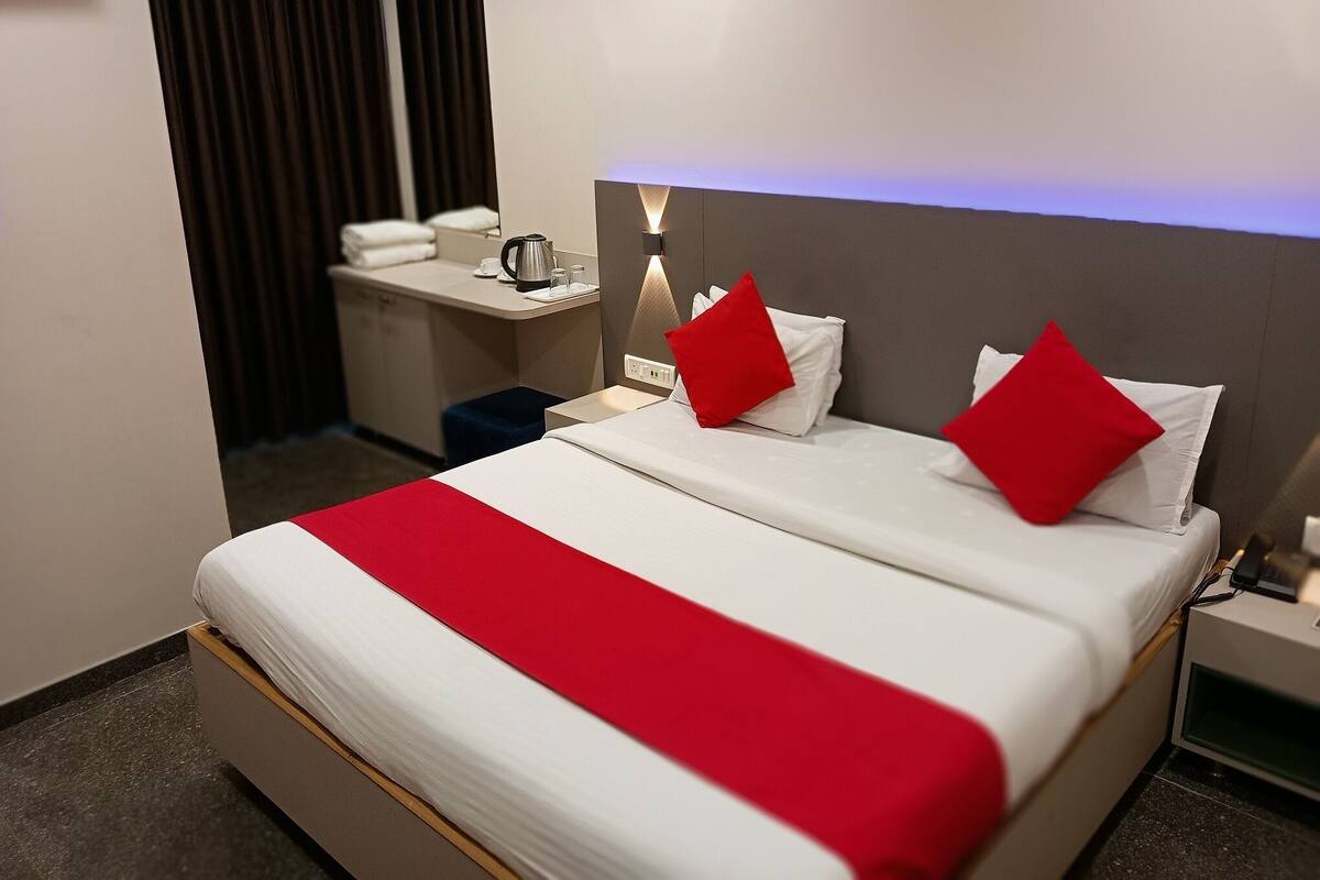 A hotel room with a bed, a bedside table, a nightstand, a desk, and a window with curtains.