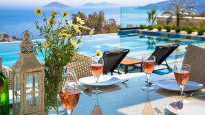 Et bord dækket til to med vinglas, en lanterne og en vase med blomster, med udsigt over en pool og havet.