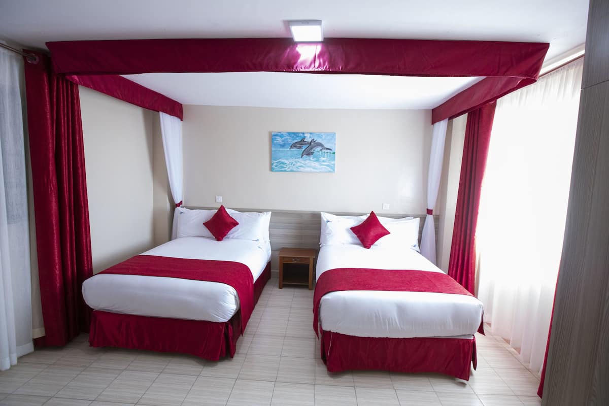 A hotel room with two beds, red curtains, white bedding, a small nightstand, and a painting on the wall.