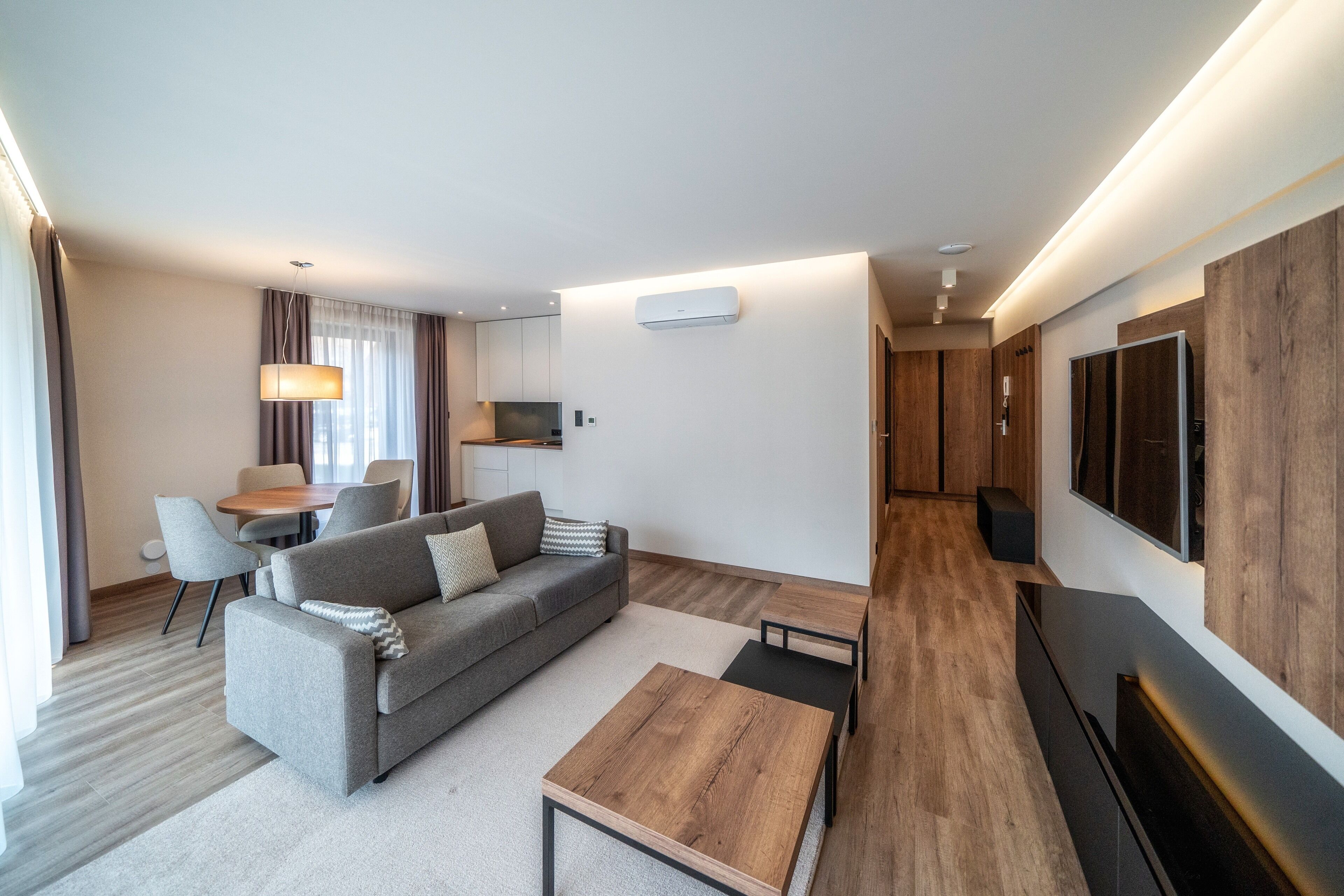 Una habitación de hotel moderna con sofá, mesa de centro, televisor y un área de comedor con sillas y una mesa.