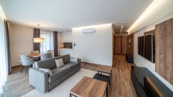 Una habitación de hotel moderna con sofá, mesa de centro, televisor y un área de comedor con sillas y una mesa.