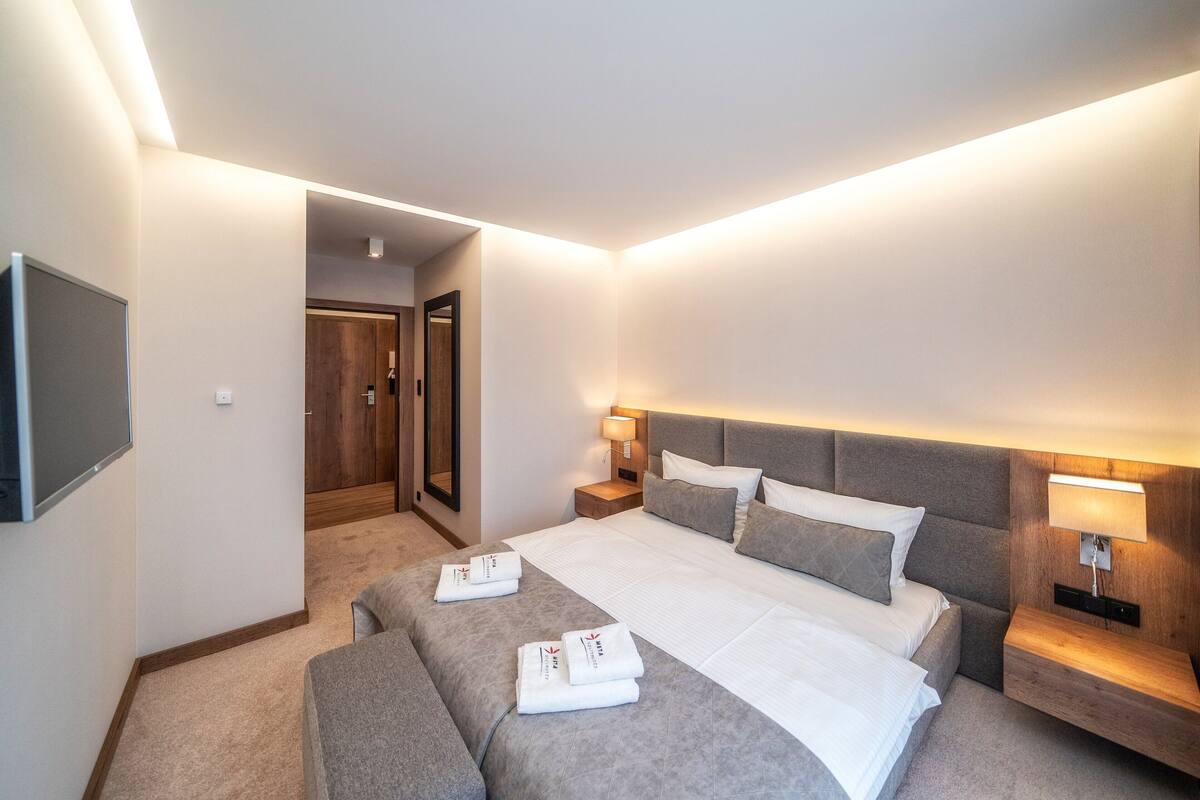 A modern hotel room with a large bed, two bedside tables, a TV, and a mirror.