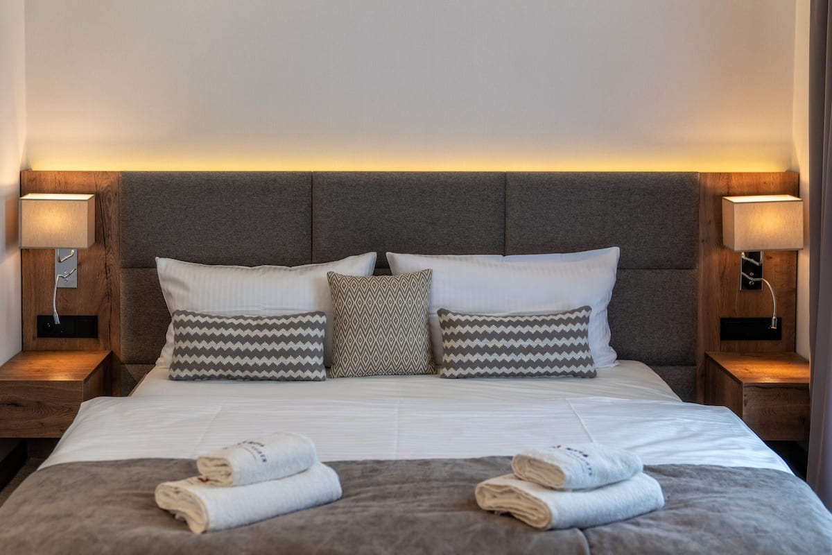 A neatly made bed with white linens and patterned pillows, flanked by wooden nightstands with lamps, in a modern hotel room.