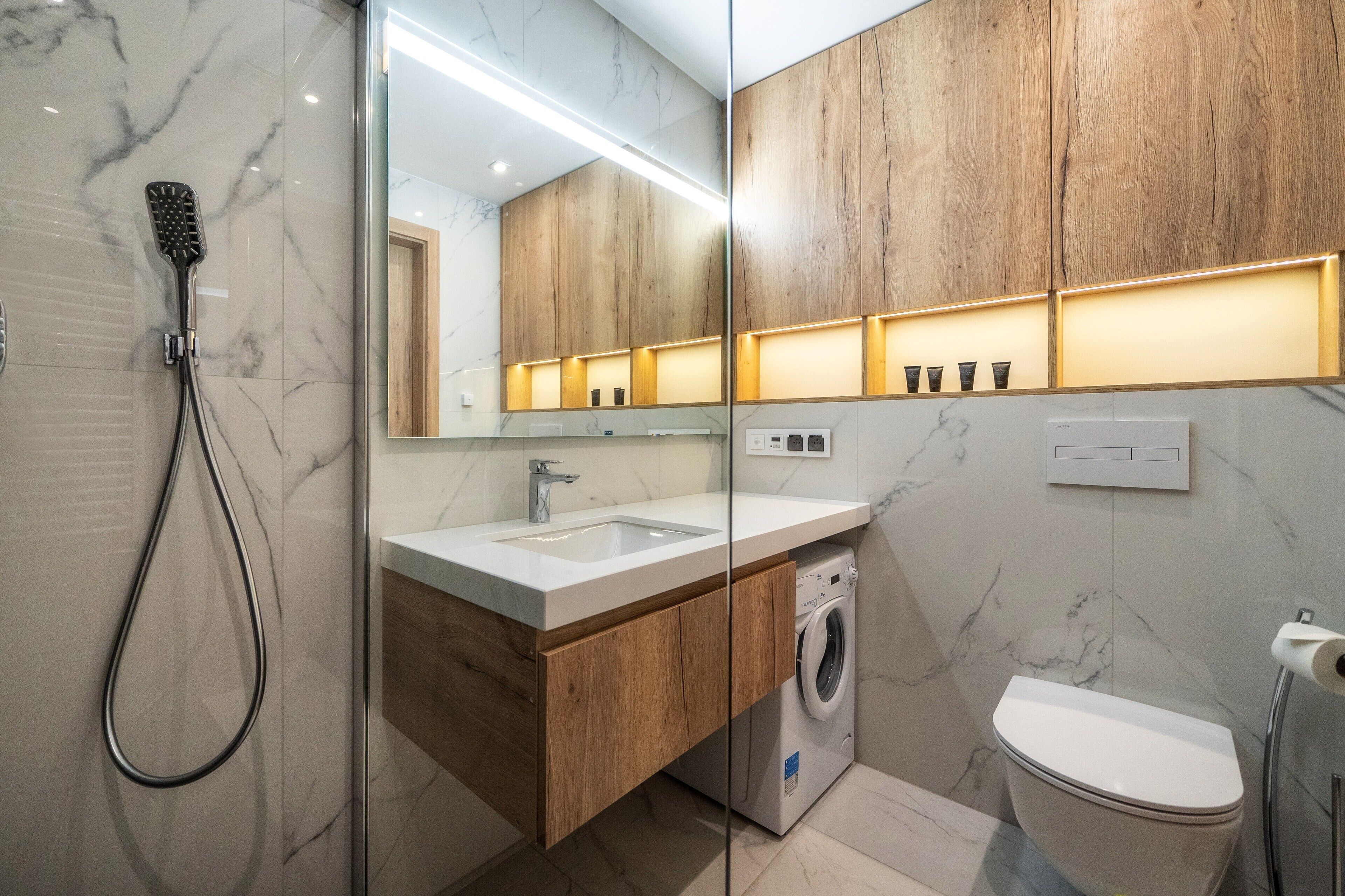 A modern bathroom with a marble backsplash, wooden vanity, a built-in washing machine, and a toilet.