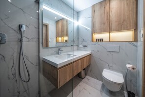 Um banheiro moderno com piso de mármore, toucador de madeira, box de vidro e vaso sanitário branco.