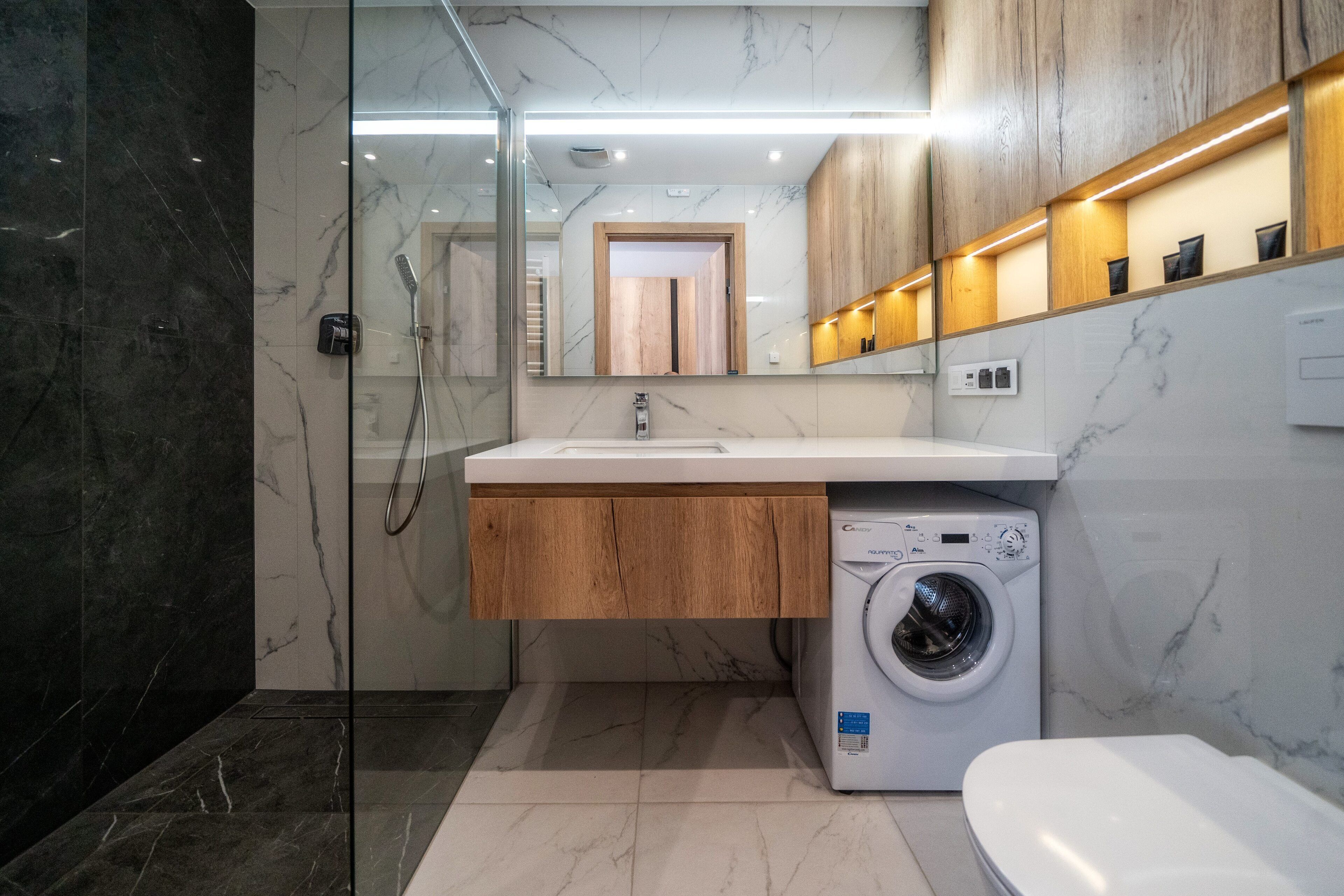 A modern bathroom with a marble vanity, a built-in washing machine, and a glass shower enclosure.