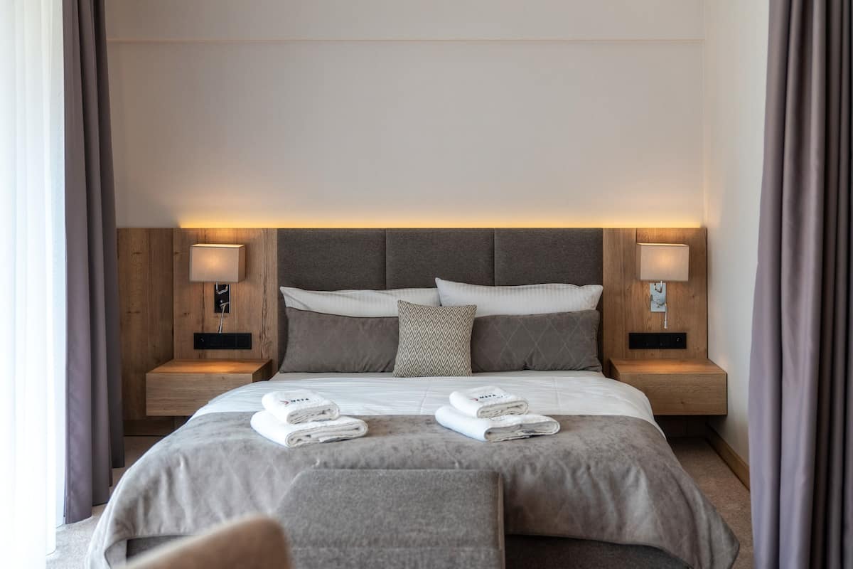 A modern hotel room with a large bed, two bedside tables with lamps, and a headboard with built-in lighting.