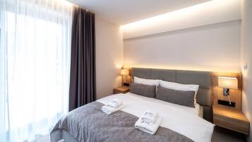 Una habitación de hotel moderna con una cama grande, dos mesitas de noche con lámparas y cortinas translúcidas en la ventana.