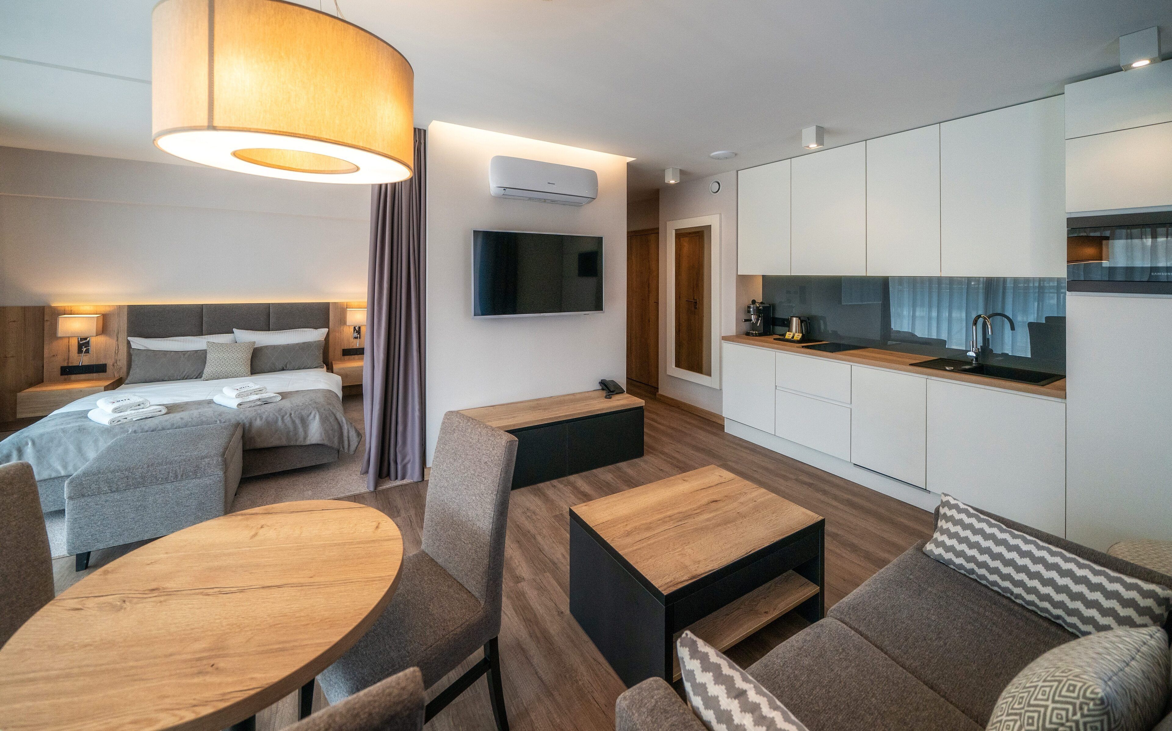 Una habitación de hotel moderna con cama, escritorio, silla, sofá, televisor y kitchenette.