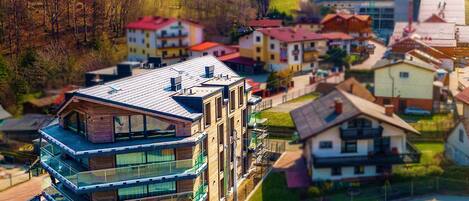 A modern building with a glass facade and a sloped roof, surrounded by residential houses with red roofs.