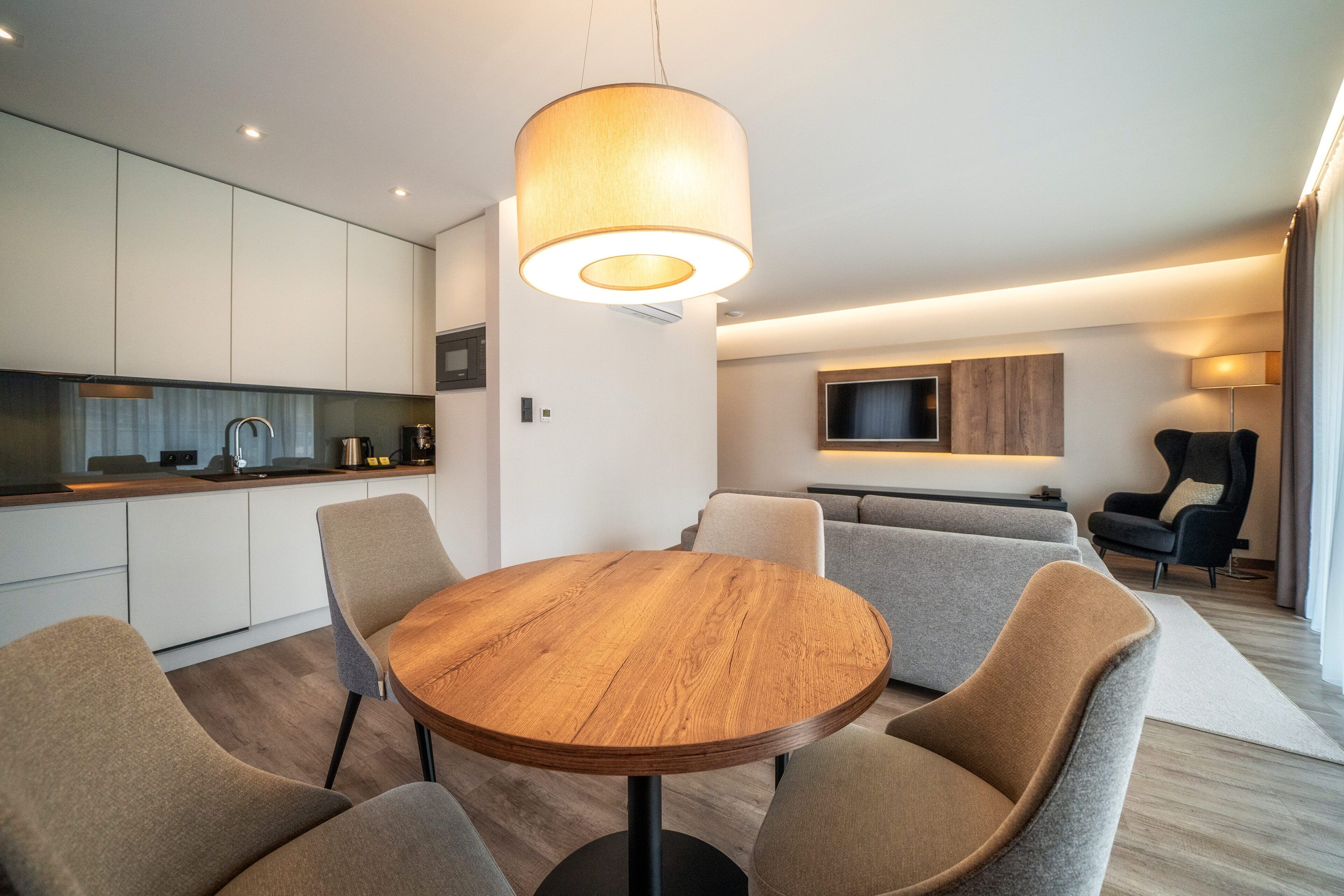 Una cocina moderna con armarios blancos, una mesa redonda de madera y cuatro sillas.