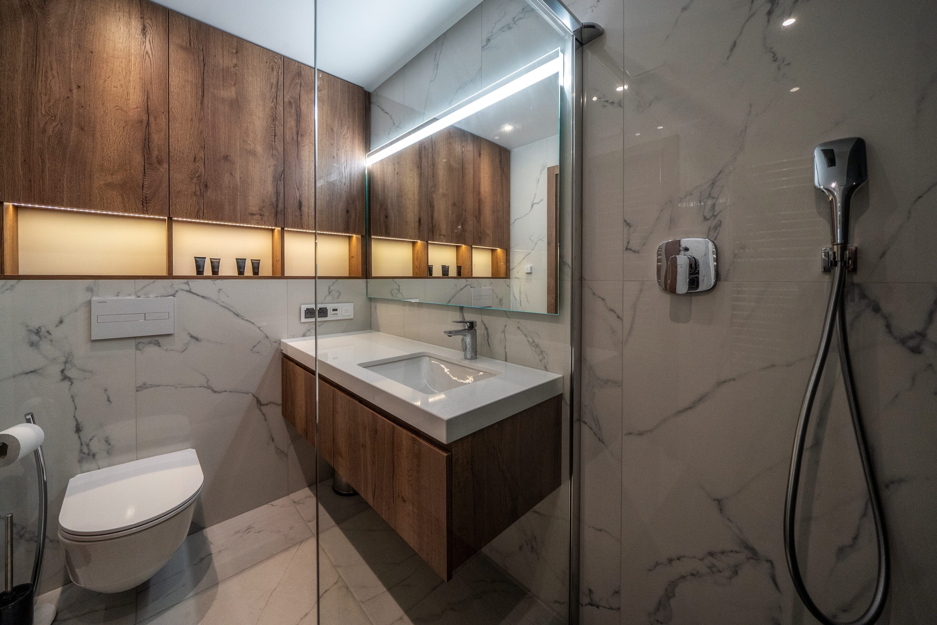 A modern bathroom with a wooden vanity, a glass shower enclosure, and a marble-tiled wall.