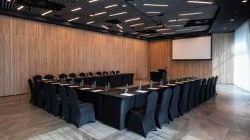 Un salón de conferencias con una larga mesa, sillas negras y una pantalla de proyector.