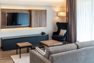 Una sala de estar moderna con un televisor de pantalla plana montado en un panel de madera, un sillón azul oscuro con un cojín, una pequeña mesa de centro de madera y un sofá gris.