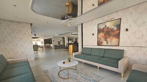 A spacious living area with a green sofa, a round coffee table, and a large abstract painting on the wall. - Snood Al Narjis Hotel (Riyadh)