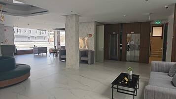 Un hall d’entrée spacieux au design moderne, comprenant un espace salon avec des canapés et une table basse, un comptoir de réception et une vue sur la rue.