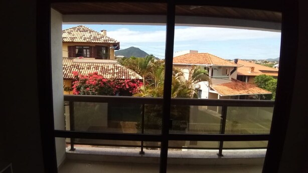 A balcony with a view of a residential area, including houses with tiled roofs and a mountain in the background. - Apartamento Praia do Santinho (Florianópolis)