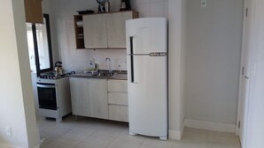 A compact kitchen with a stove, sink, and white refrigerator. - Apartamento Praia do Santinho (Florianópolis)