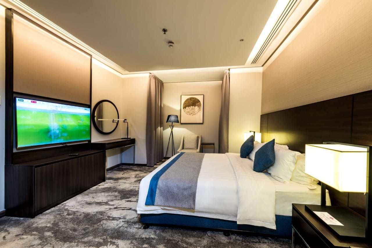 Une chambre d’hôtel dotée d’une grande télévision à écran plat, d’un lit recouvert d’une couverture à rayures bleues et blanches, d’une table de chevet avec une lampe et d’un lampadaire.