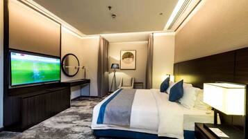 Une chambre d’hôtel dotée d’une grande télévision à écran plat, d’un lit recouvert d’une couverture à rayures bleues et blanches, d’une table de chevet avec une lampe et d’un lampadaire.