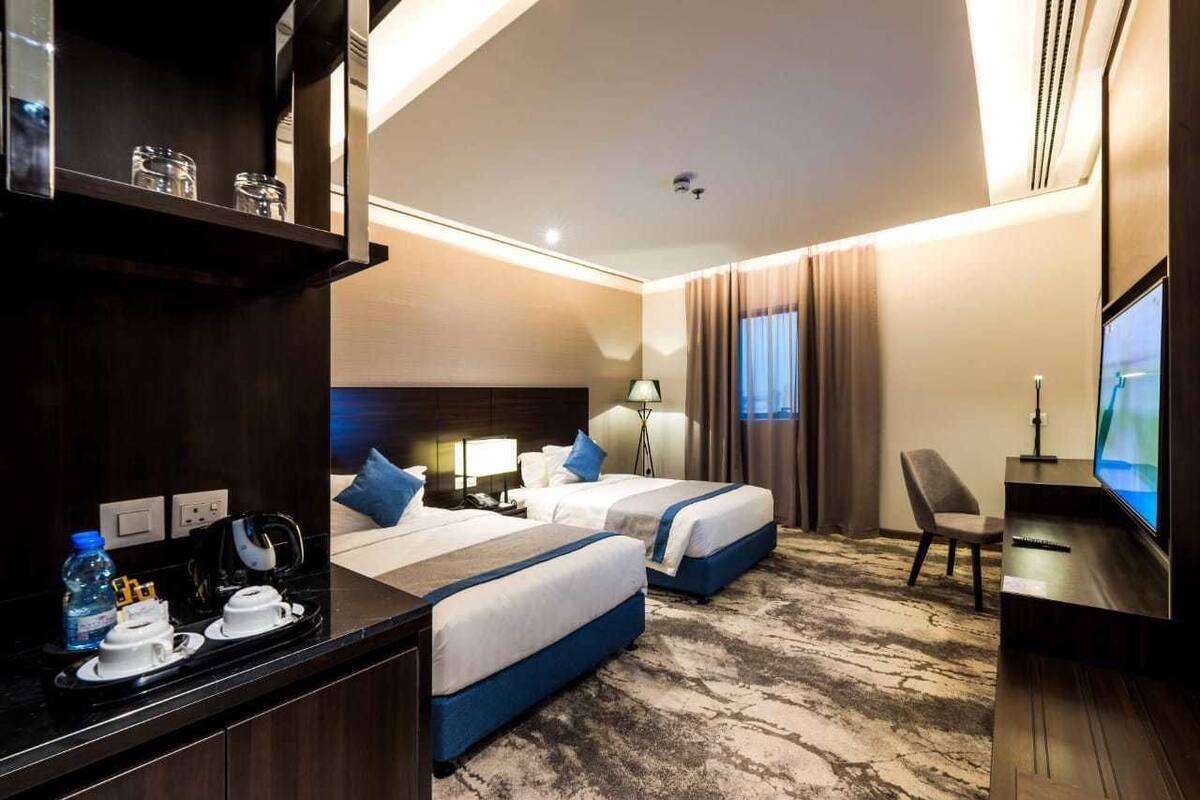 A hotel room with two beds, a desk, a television, and a minibar.