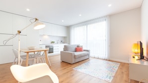 A modern living space with a dining area, a sofa, a TV, and a kitchen in the background.