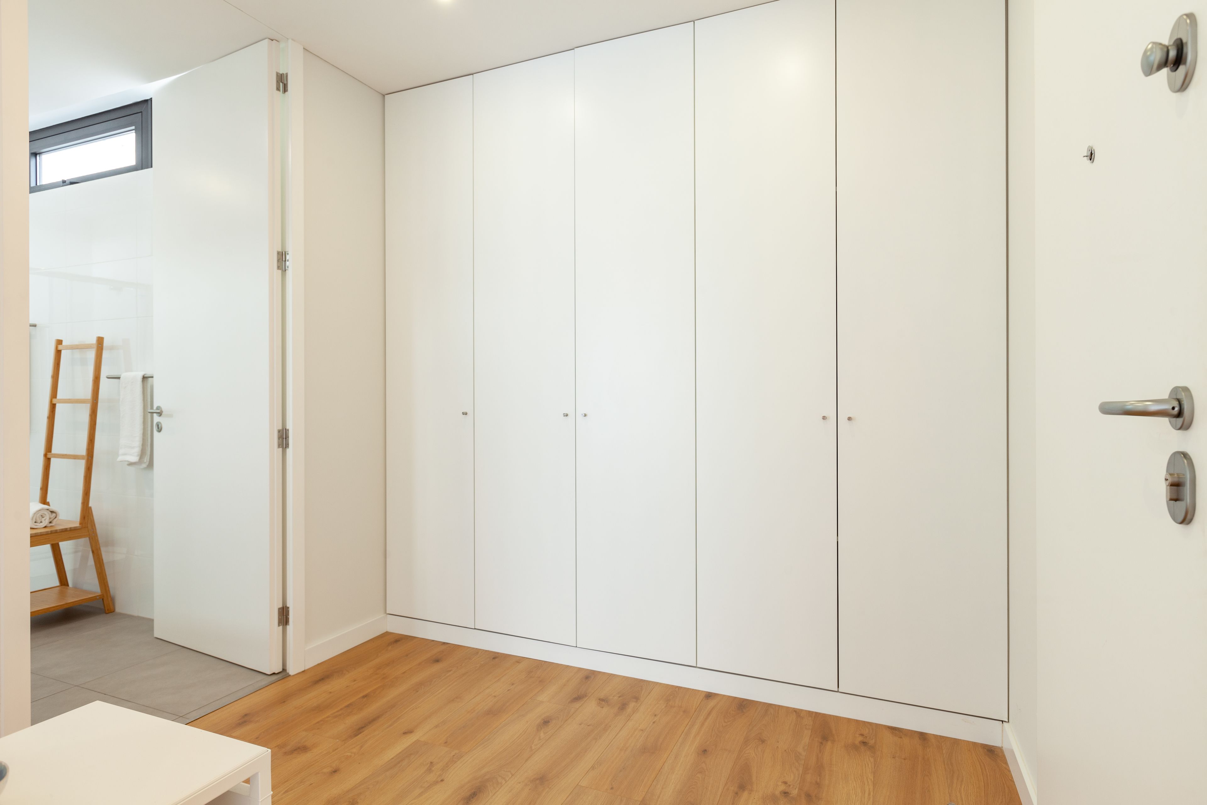 A room with a wooden floor, white wardrobe, and a wooden ladder leaning against the wall.