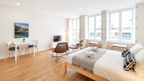 A modern hotel room with a large bed, a desk with a TV, two chairs, and a painting on the wall.