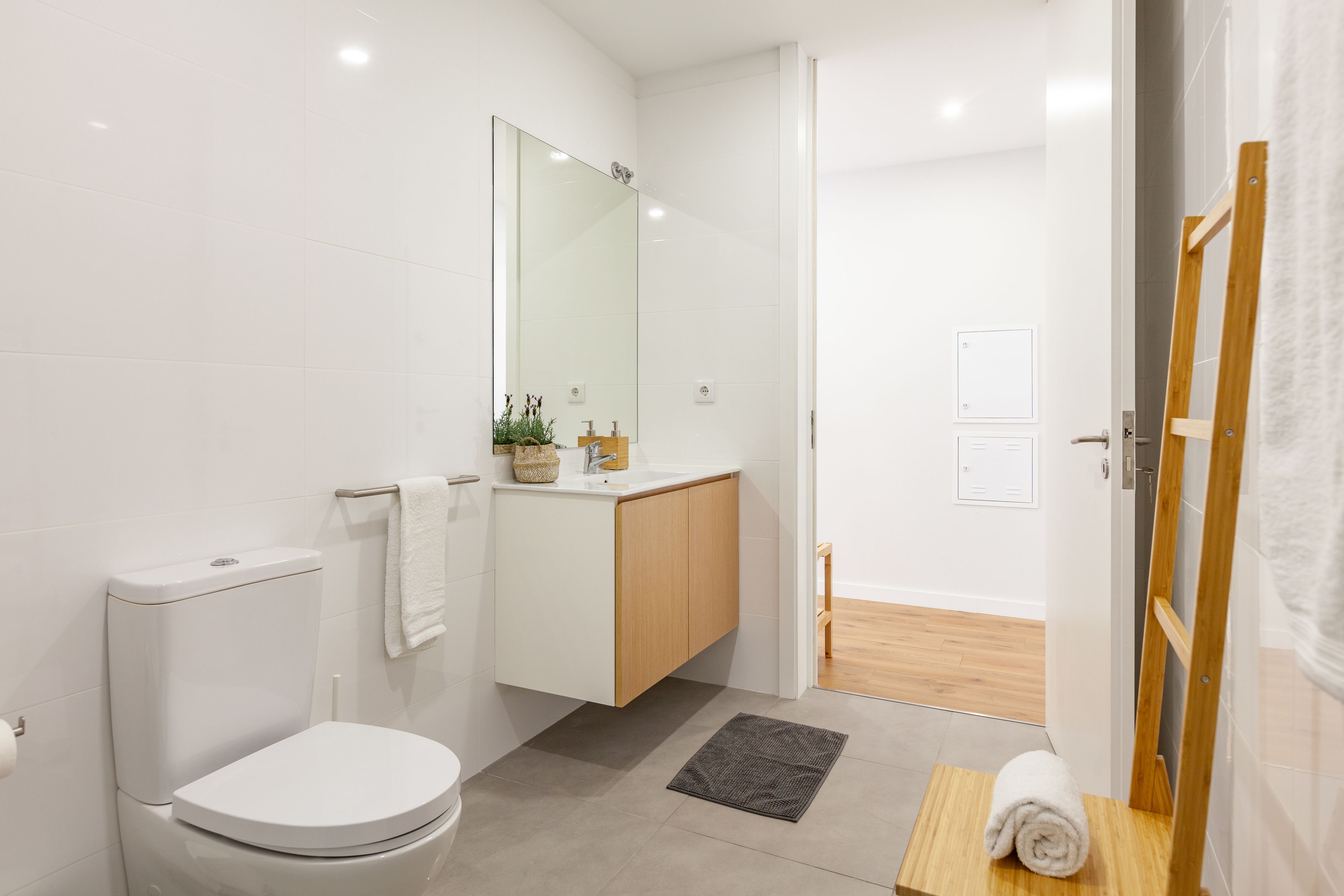 A modern bathroom with a toilet, sink, mirror, and wooden cabinet.