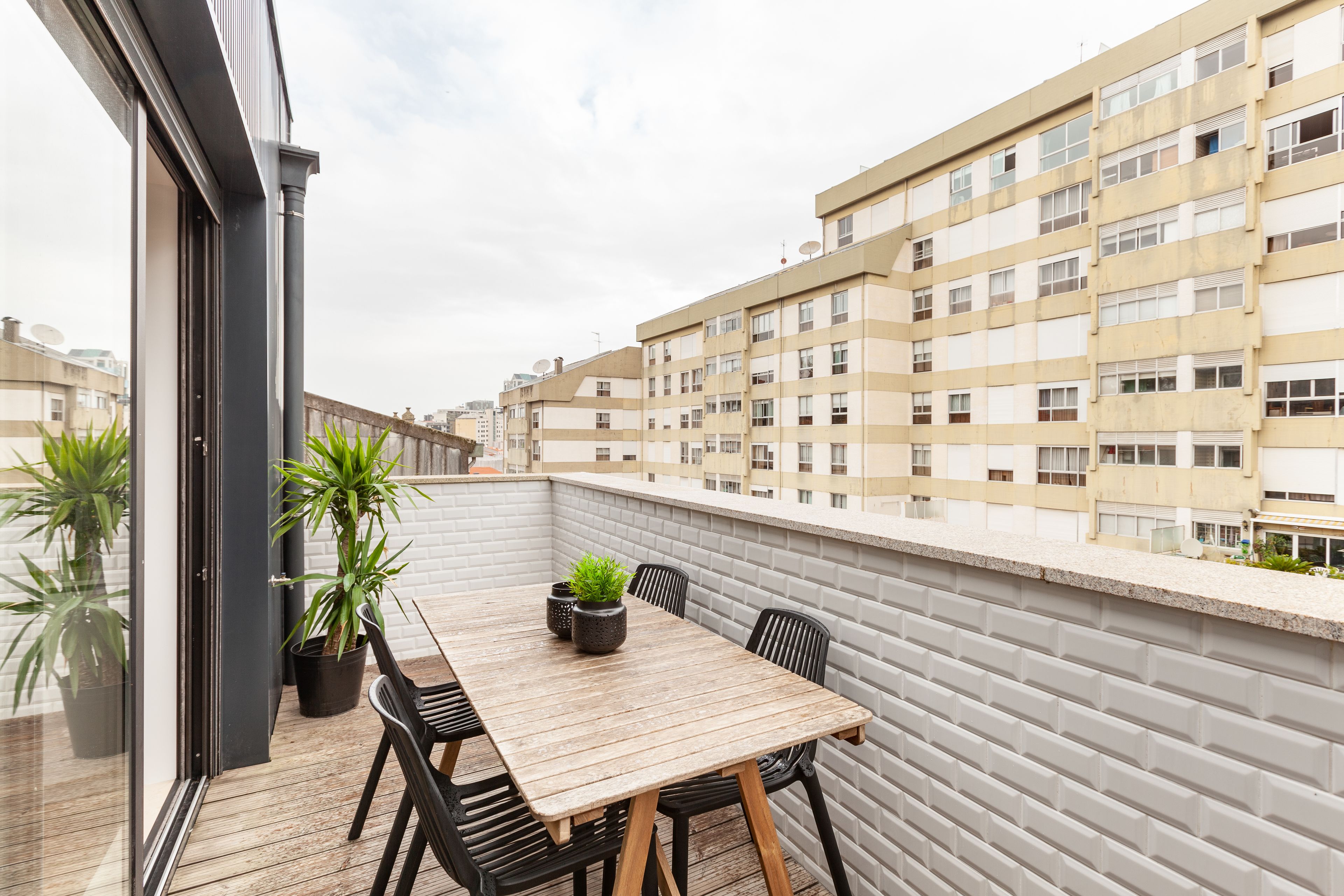 Ein Balkon mit Holztisch und -stühlen, Blumentöpfen und Blick auf benachbarte Gebäude.